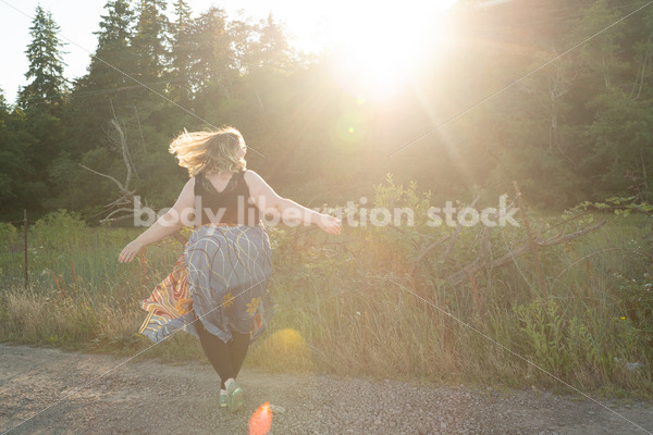 Joyful Movement Stock Image: Plus-Size Woman Twirls on Rural Road at Golden Hour - Body Liberation Photos